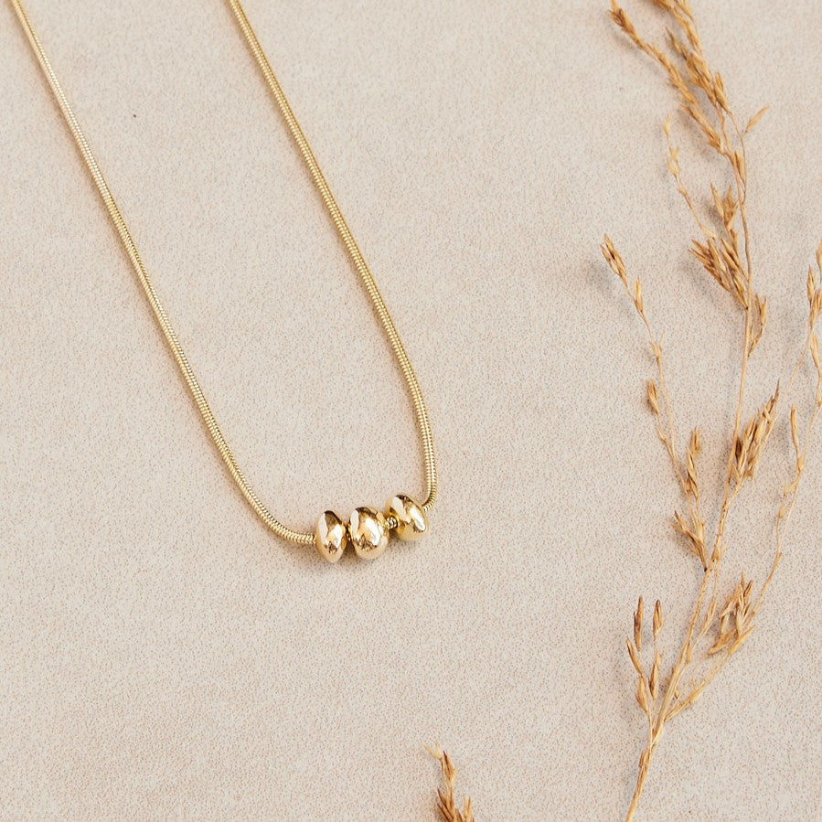 14 karaat gouden  hanger Essentials: 3  minimalistische organische gouden steentjes aan een ketting. Liggend op een stenen ondergrond met een gedroogd takje ernaast.