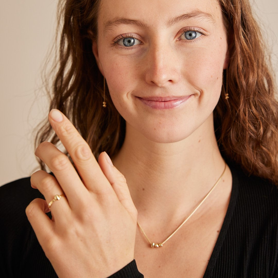 Model draagt Essentials collectie, minimalistische organische gouden steentjes van 14 karaat goud aan een ketting, oorhangers en ring.