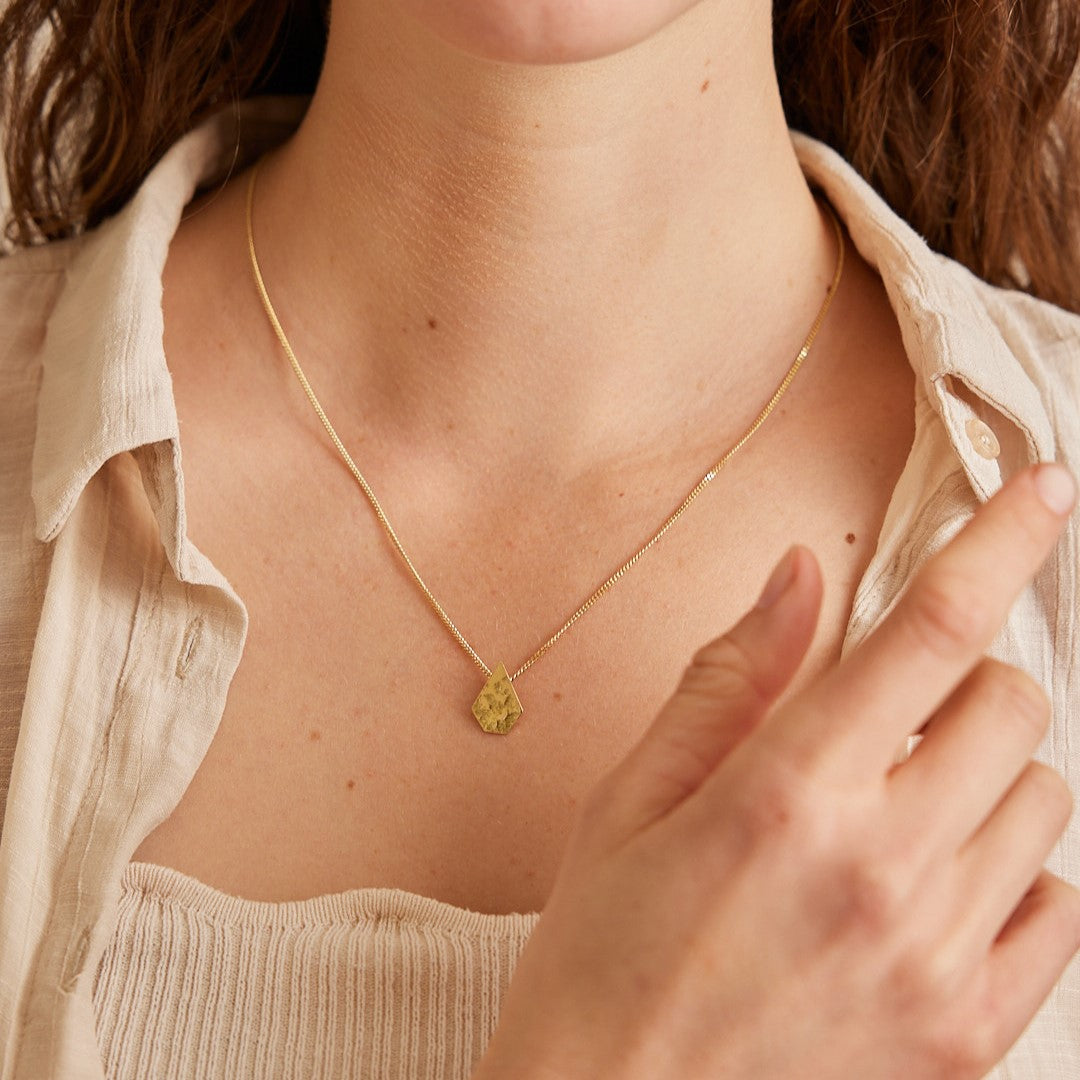 Hals van model dat ketting draagt met 18 K geelgouden hanger "Imperfectie Rocks". En haar hand voorlangs in beeld.