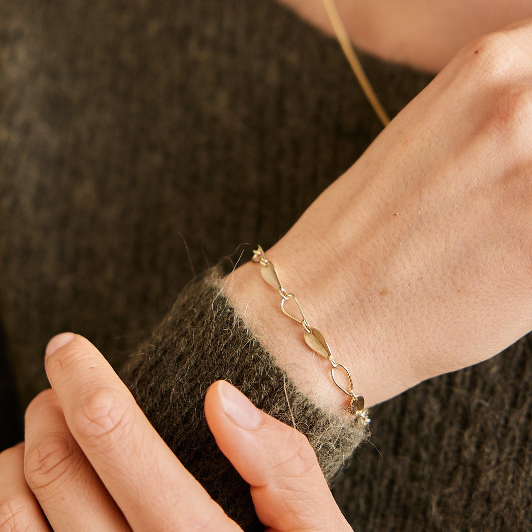 Gouden armband Leaves met afwisselend open en dichte blaadjes. Gedragen om de pols van een model met groene trui aan.