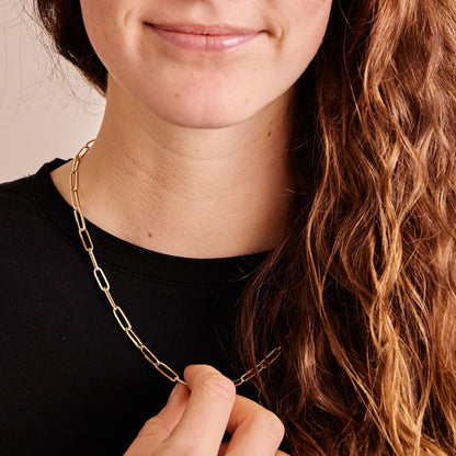 Model met zwart t-shirt draagt een 14 karaat gouden schakelketting van de collectie Verbondenheid. De paperclipschakels staan symbool voor verbinding.